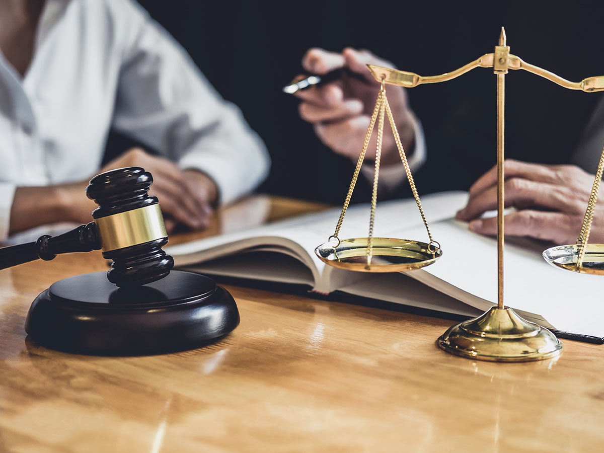 Two people sit at a table with a gavel and scales in the foreground